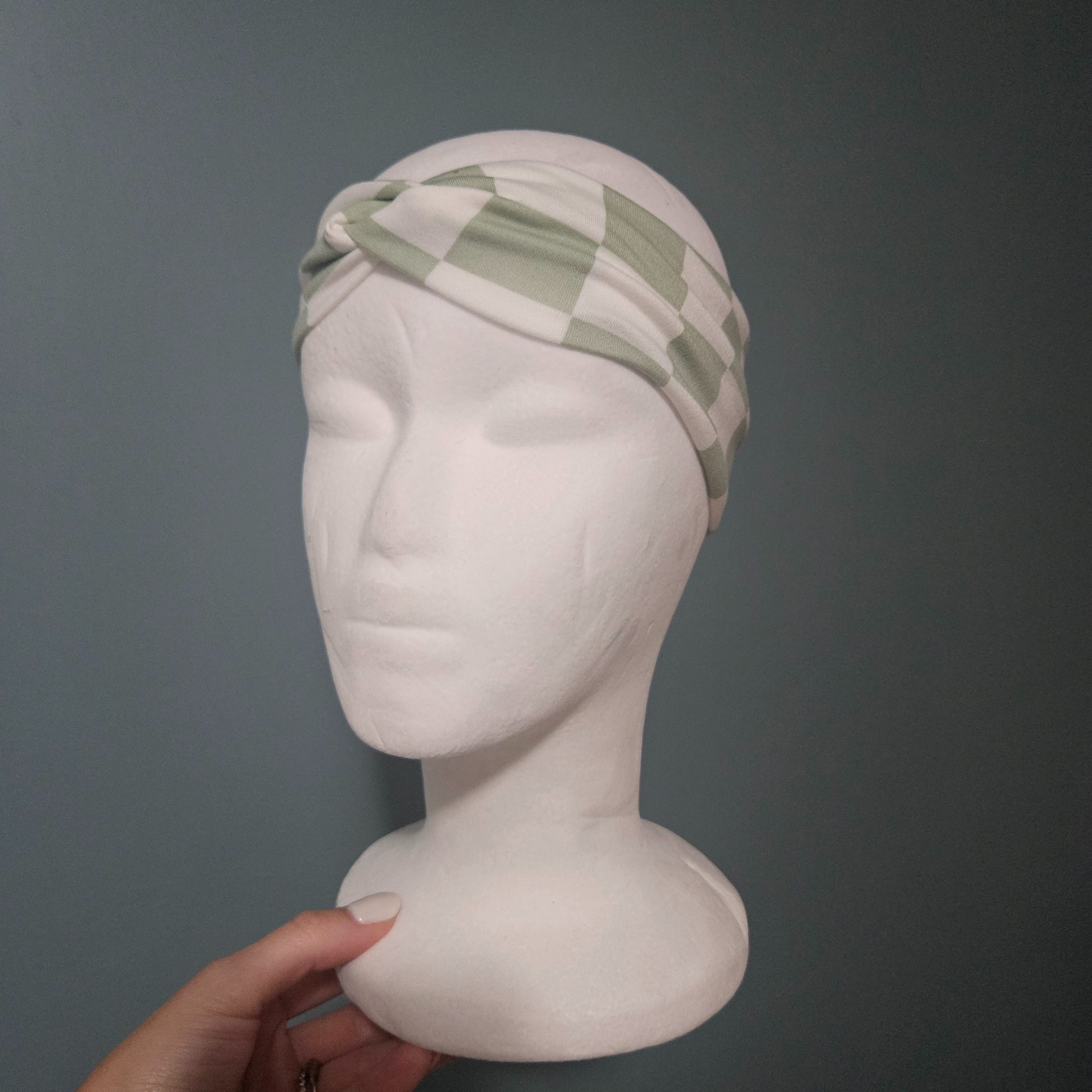 Green and white checkered headband on a mannequin head against a gray background
